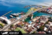 Pemandangan udara Kota Manado di atas menampilkan Jembatan Soekarno yang ikonik, Pelabuhan Manado yang sibuk dengan deretan kapal, serta kawasan pemukiman dan bisnis yang padat di sepanjang pesisir. Gambar ini adalah potret visual yang sempurna dari geliat ekonomi dan pembangunan infrastruktur di ibukota Provinsi Sulawesi Utara tersebut.