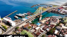Pemandangan udara Kota Manado di atas menampilkan Jembatan Soekarno yang ikonik, Pelabuhan Manado yang sibuk dengan deretan kapal, serta kawasan pemukiman dan bisnis yang padat di sepanjang pesisir. Gambar ini adalah potret visual yang sempurna dari geliat ekonomi dan pembangunan infrastruktur di ibukota Provinsi Sulawesi Utara tersebut.