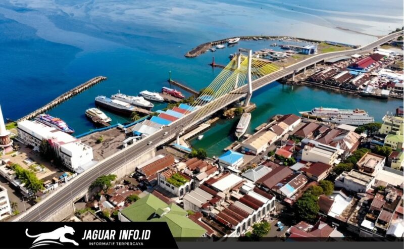 Pemandangan udara Kota Manado di atas menampilkan Jembatan Soekarno yang ikonik, Pelabuhan Manado yang sibuk dengan deretan kapal, serta kawasan pemukiman dan bisnis yang padat di sepanjang pesisir. Gambar ini adalah potret visual yang sempurna dari geliat ekonomi dan pembangunan infrastruktur di ibukota Provinsi Sulawesi Utara tersebut.