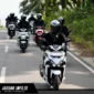 Ilustrasi pengendara motor menggunakan helm bervisual tertutup dan masker sebagai perlengkapan keselamatan saat menghadapi hujan abu vulkanik di jalan raya.